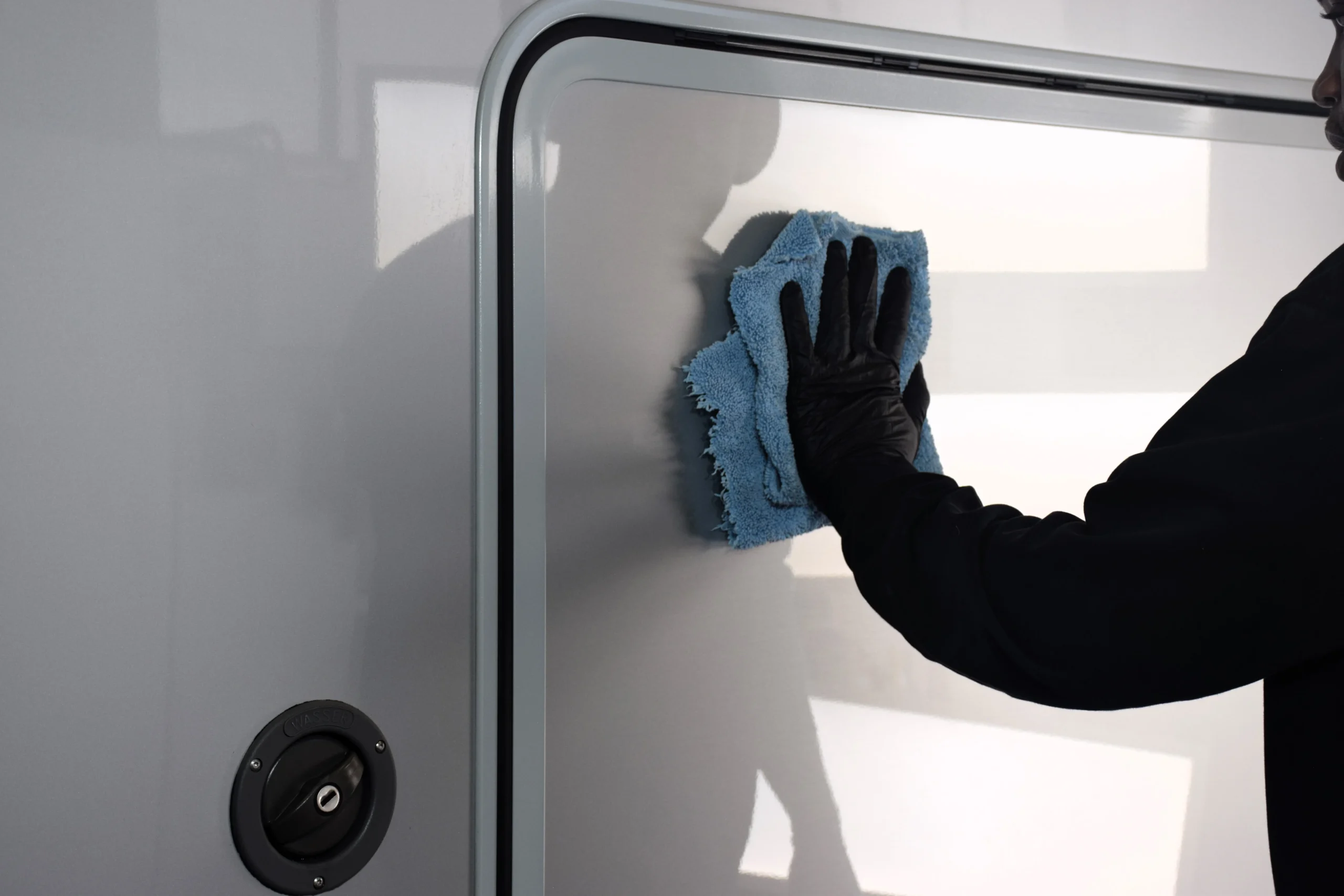Person wischt mit einem Lappen über die Oberfläche eines Wohnmobils- Camperforyou Außenreinigung